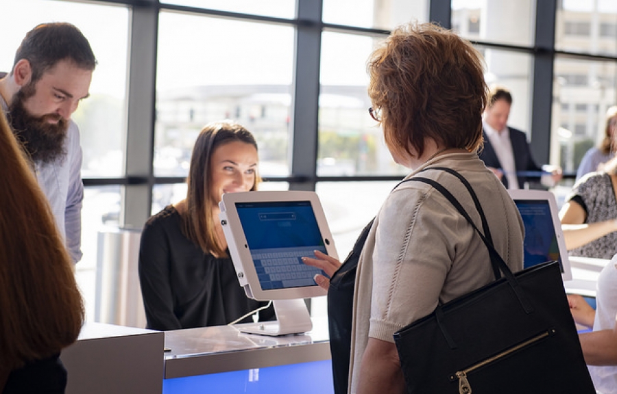 Woman using a touch screen while a man waits in line behind her at a convention.