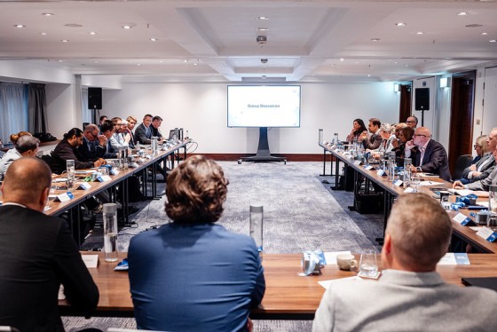 People gathered in conference room with projector screen and tables, discussing with the text "Group Discussion" on the screen.