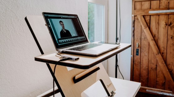 Laptop on a stand recording a webinar with a man in the screen and a wooden door in the background.