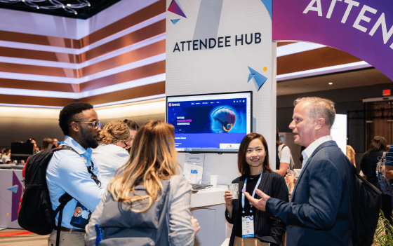 People standing around the attendee hub sign with a monitor in front of them at a convention.