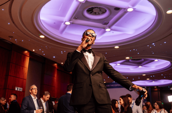 A man wearing a tuxedo sings on stage at an event in the Radisson Blu Hotel.