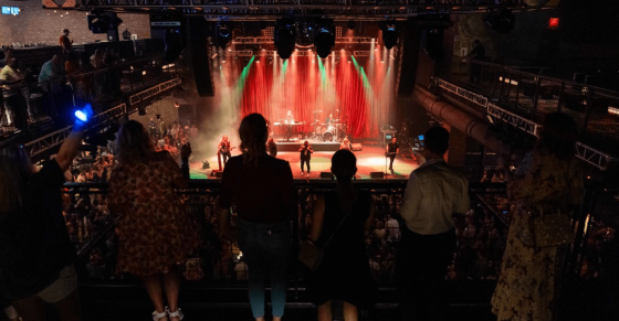 Crowd of people looking at a band on a stage with a red curtain at the music pub.