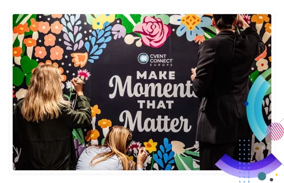 Two women paint a mural for Cvent Connect Europe with a message that says, "Make Moments That Matter."