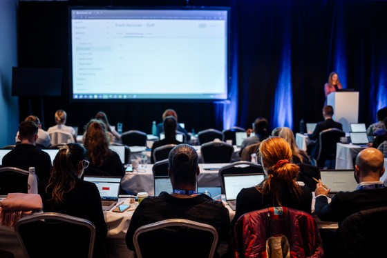 Audience tuned in to a presentation on a screen at the front of the room.