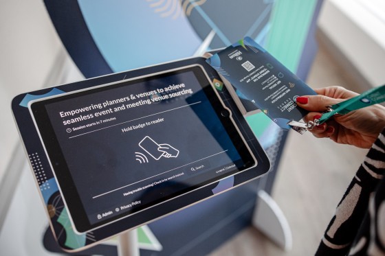 A woman holding a badge next to a touch screen device with an event screen on it.