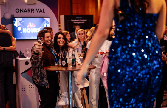 People at an event with a large ONARRIVAL sign and monitor displaying After Hours.