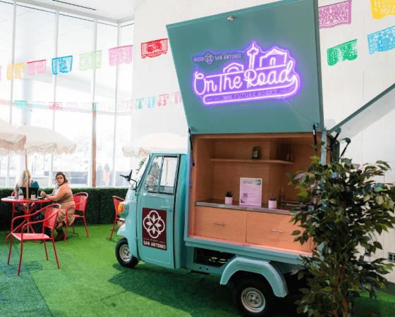 Truck with neon "On The Road" text in front of wall with colorful paper banners.