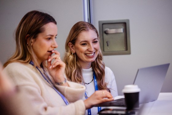 Two women laughing and working on a laptop at Cvent CONNECT 2024 in London.