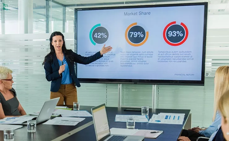 A woman in an office is showing the market share data on a screen to other people.