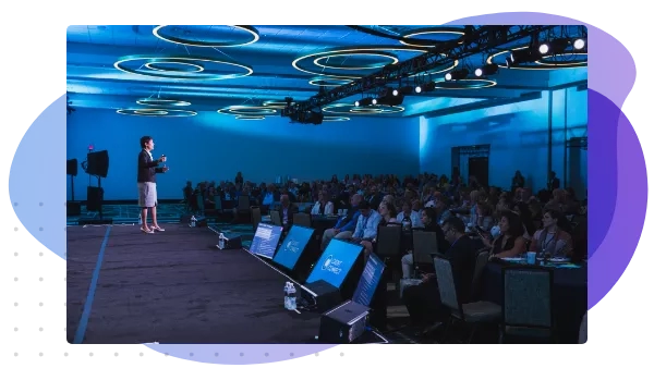 A woman gives a presentation on stage to a large crowd of people.