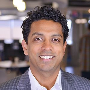 Headshot of Pradeep Mannakkara smiling at the camera with an office in the background.