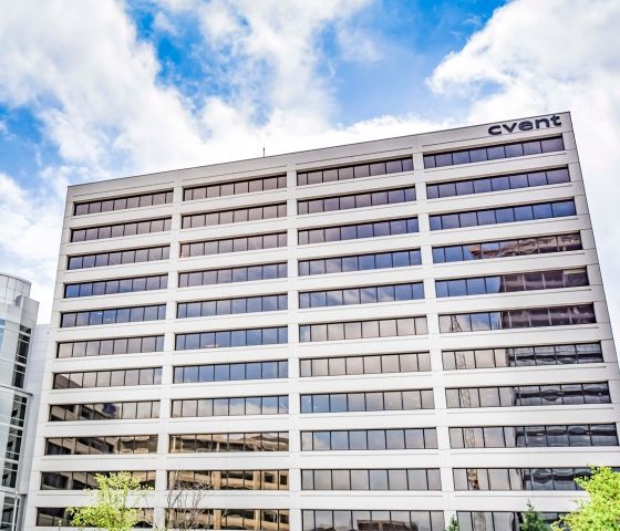 Cvent office building with glass windows, trees, and a blue sky with clouds on a sunny day.