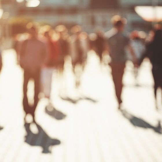 A group of people walking on the sidewalk, with blurred images of architecture, landscaping, and ambiance.