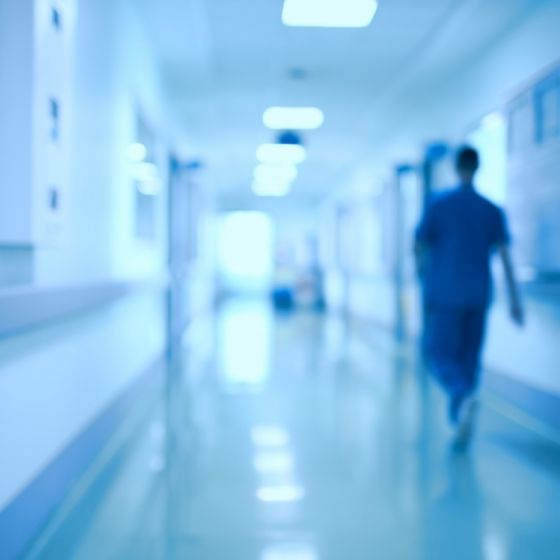 A blurry photo of a hospital hallway with a person in blue walking towards the end.