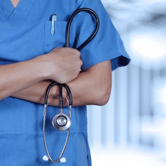 Nurse in blue scrubs with stethoscope over her shoulder in a hospital corridor.