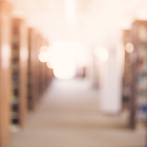 Blurry image of a library with a pathway and rows of bookshelves on either side.