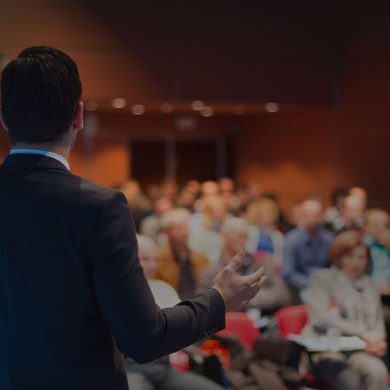 A man standing on a platform in front of an audience in a conference room.
