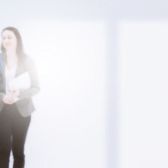 A group of business people are standing and discussing something in front of a blurry white wall.