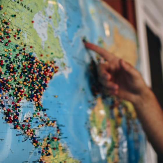 A person is pointing at a world map with pins placed on various countries.