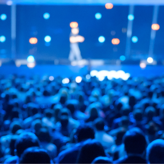 Large crowd of people gathered in a venue with blue and orange lights on the ceiling.