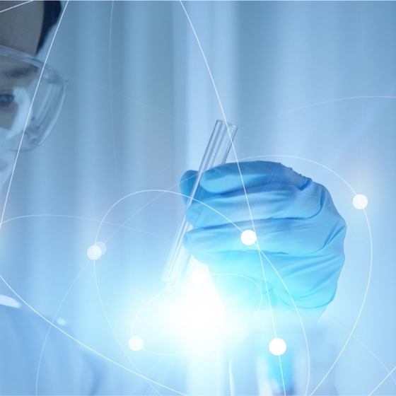 A scientist in PPE holds a test tube emitting light with an abstract blue background.