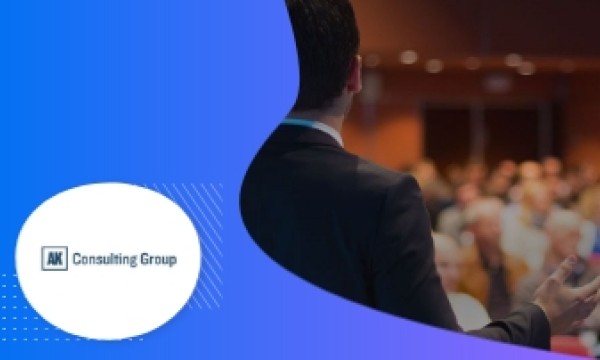 A man in a suit is giving a presentation at a conference for the AK Consulting Group.