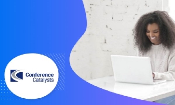 A woman is working on a laptop on a table with the Conference Catalysts logo nearby.