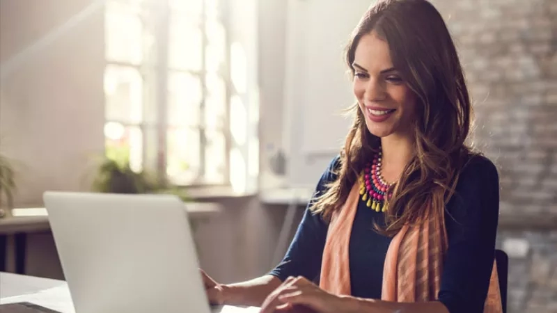 A smiling woman using a laptop at a desk in an office