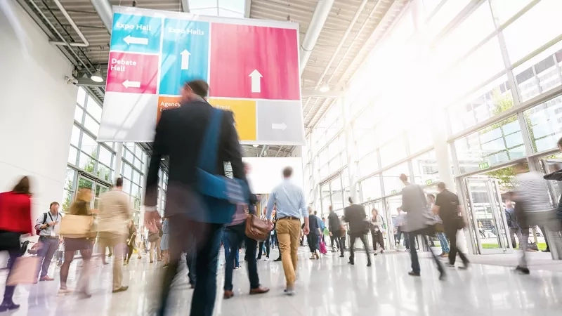 Several people walking in a crowded room with a banner on top that reads "Expo Hall" and "Debate Hall."