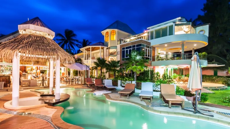 Nighttime view of luxury hotel with pool, cabanas, and lush landscaping, exuding a serene and inviting ambiance.