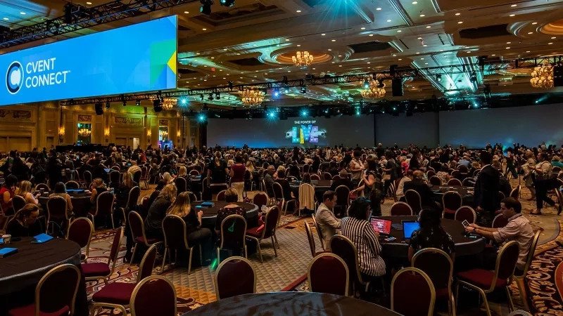 A conference room with round tables and chairs, a large screen, and a chandelier, titled "Cvent Connect General Session 2018".