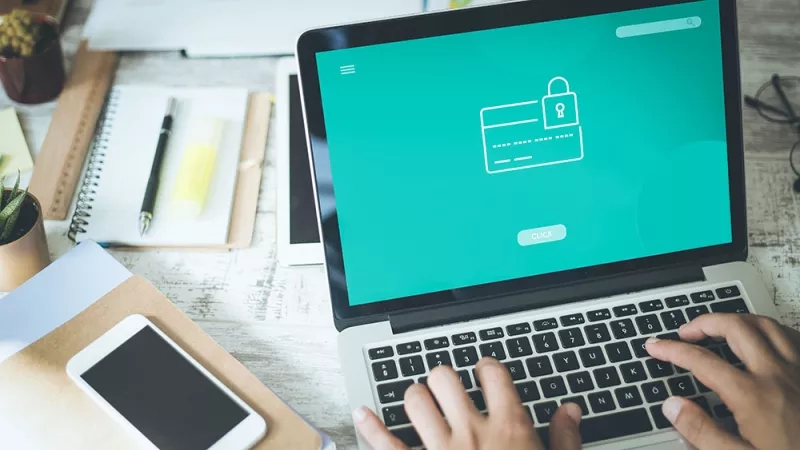 Person typing on laptop with a green screen showing a credit card and lock icon.