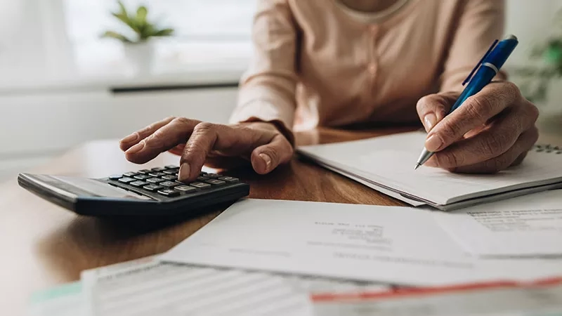 A woman calculating her budget on a calculator with papers and a pen in front of her.