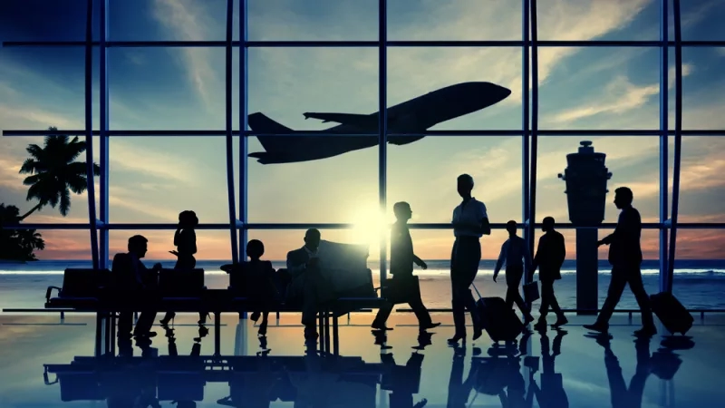 Silhouette of travelers in an airport terminal with a plane taking off in the background.