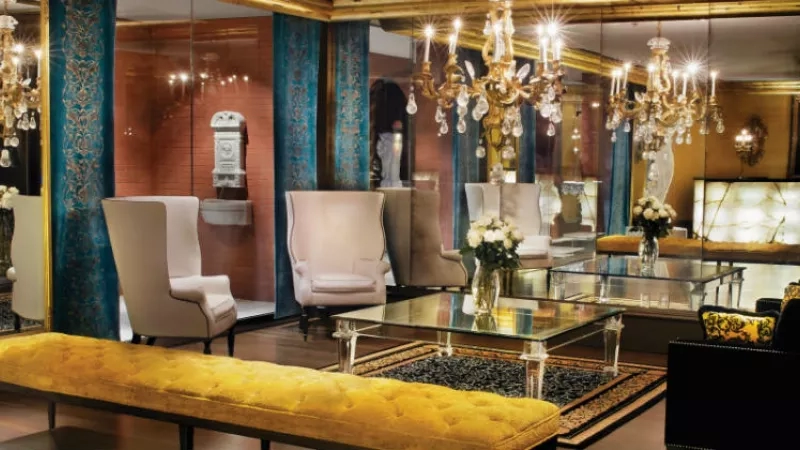A luxurious interior with a yellow bench, a glass table, and chandeliers, reflecting elegance and opulence.