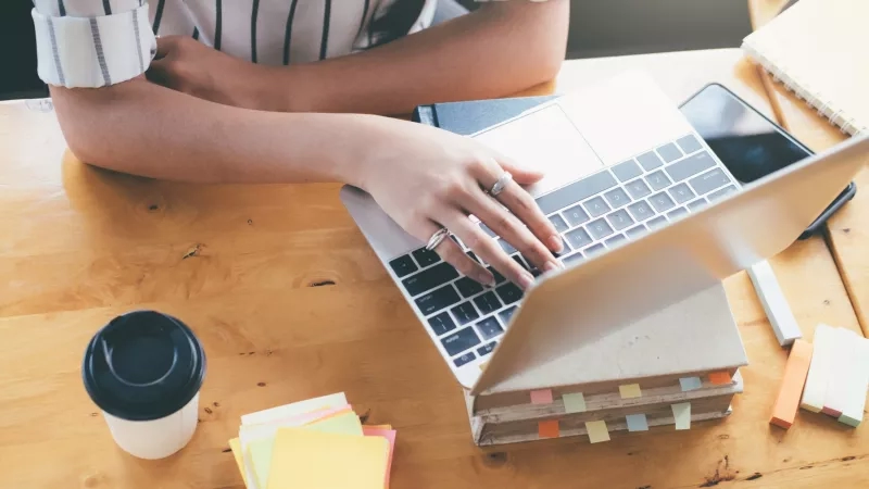 Woman typing on a laptop with sticky notes and a cup of coffee on the table.