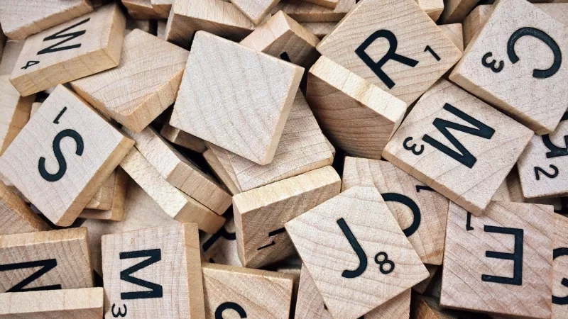Wooden alphabets, letters, and tiles for Scrabble game with numbers and letters on them, placed in a pile.