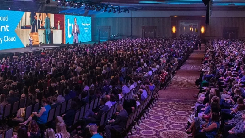 A large crowd of people are gathered in a conference hall for the Oracle CloudWorld event.