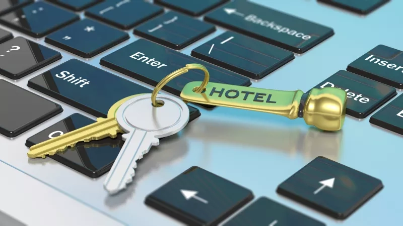 Two hotel room keys with key tag on top of computer keyboard with word hotel on key tag.