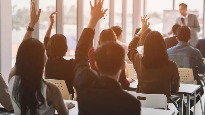 A group of students in a classroom raising their hands to ask a question during a lecture.