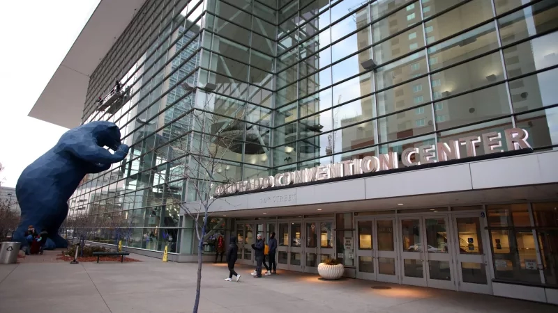 The Colorado Convention Center with large blue bear sculpture and people walking around the entrance.