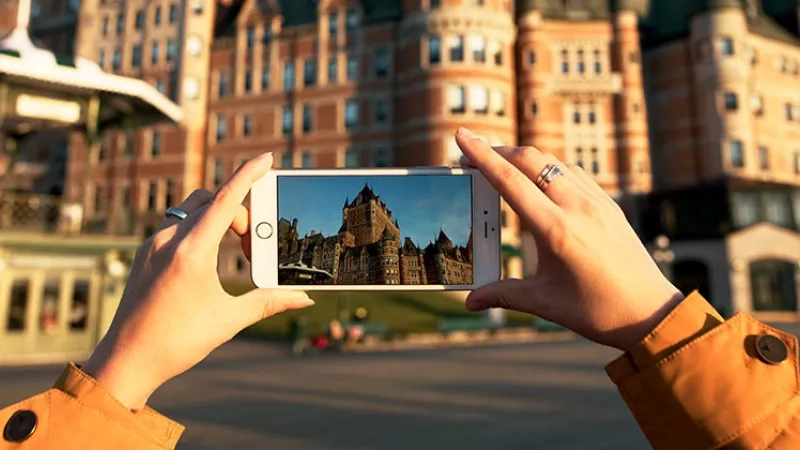 A person is capturing the Fairmont Chateau Laurier with a cellphone camera in front of the hotel.