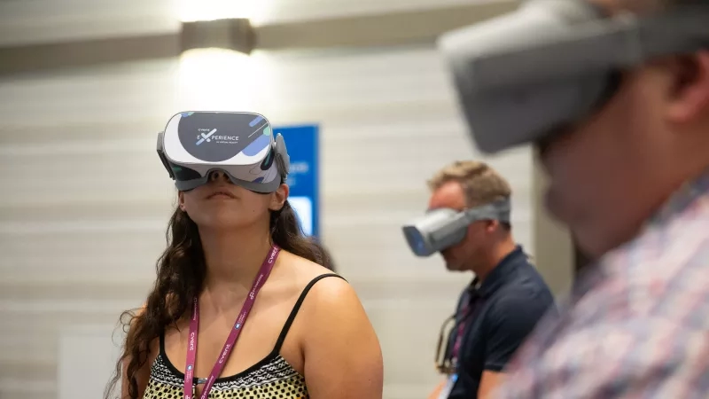 Two people with VR headsets on at an event with a blurred background and a sign.