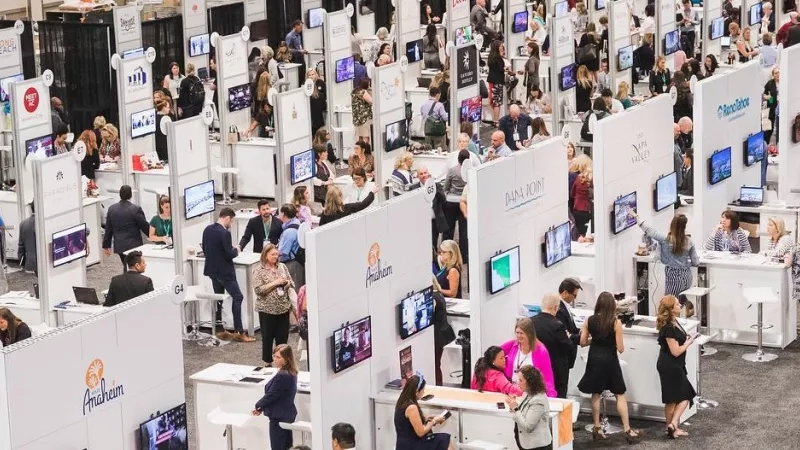 An aerial view of a busy convention with people standing in front of booths and some looking at monitors.