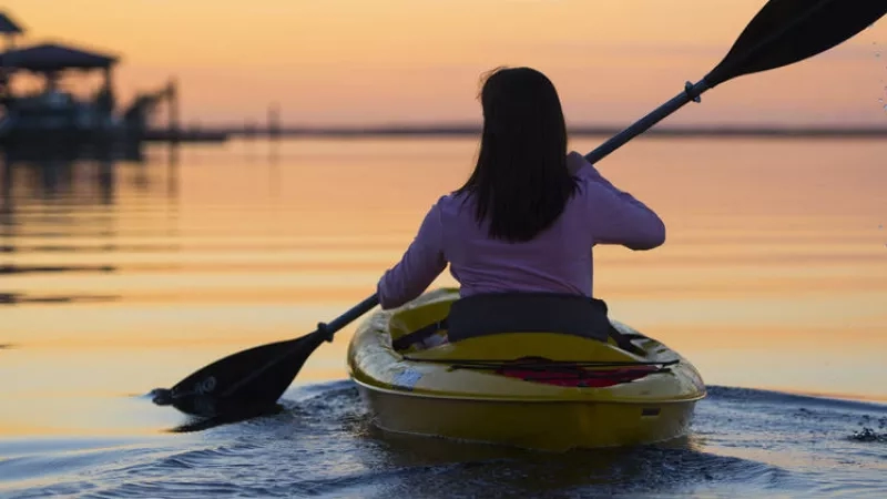 A woman kayaking at sunset, enjoying the peaceful ambiance of the calm water and the vibrant sky.