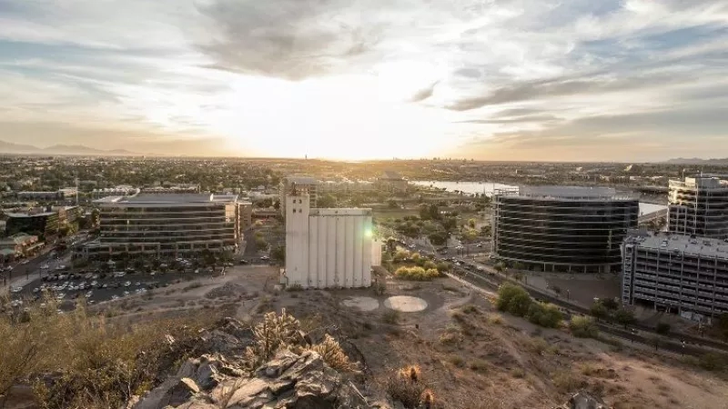 Panoramic view of Scottsdale, Arizona, with buildings and a lake under a sunset sky.