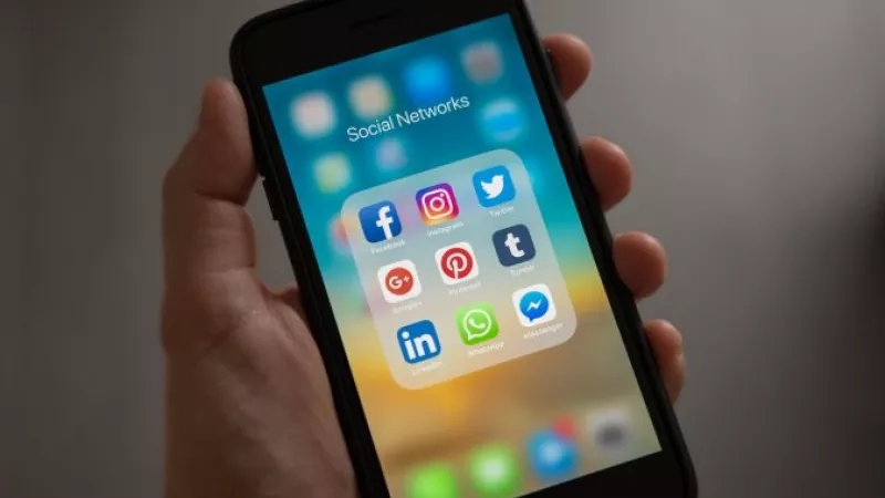Person holding a cell phone with social media icons on the screen.