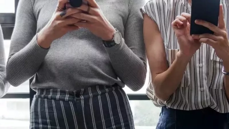Four people standing in front of a glass window, each holding a cell phone in their hands.