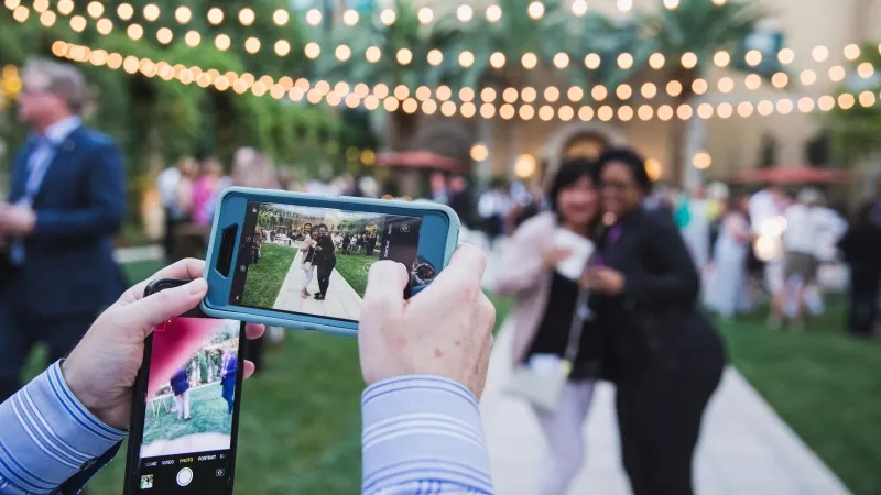 Two people take photos of a bride and groom at an outdoor wedding reception at The Palms Hotel.