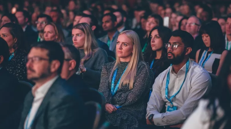 A group of people are sitting in a conference hall and looking forward at the speaker.